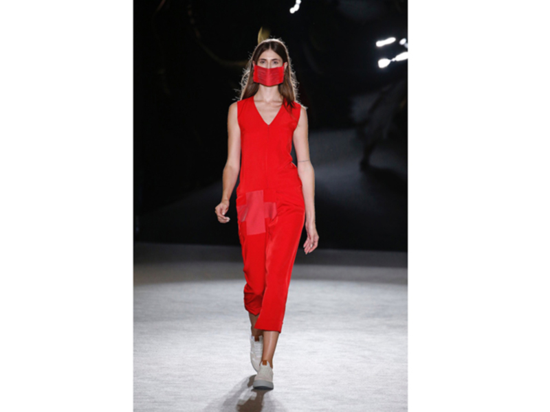 Modela con traje rojo y máscara en desfile de moda.