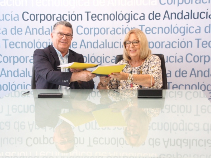 Dos personas sosteniendo un documento en una reunión formal. El fondo está borroso con letras en español, probablemente relacionadas con la corporación tecnológica de Andalucía.