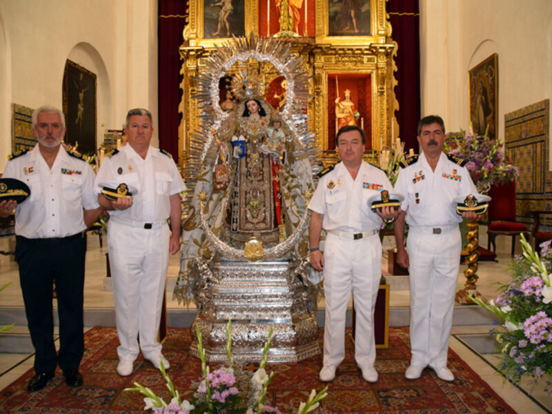 Oficiales en uniforme blanco posan frente a una imagen religiosa ornada en un interior de iglesia.