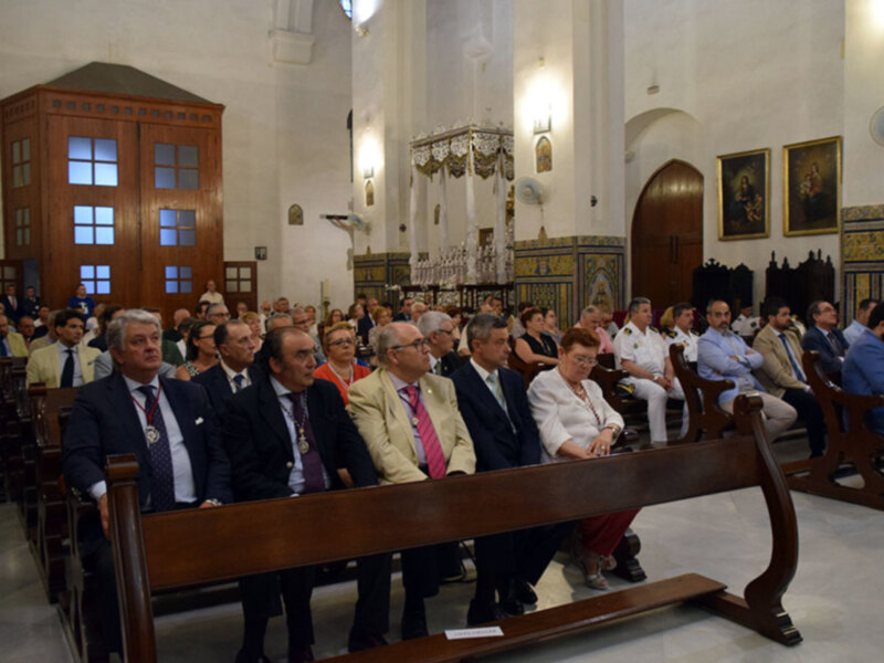 Una reunión formal en una iglesia con personas vestidas formalmente sentadas en bancos de madera.