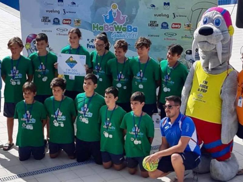 Equipo de natación infantil posando con su mascota y medallas en la piscina.