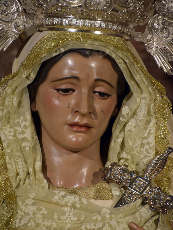 Imagen de la Virgen María con un velo dorado y una corona de plata, sosteniendo una espada. La imagen muestra una escena religiosa.