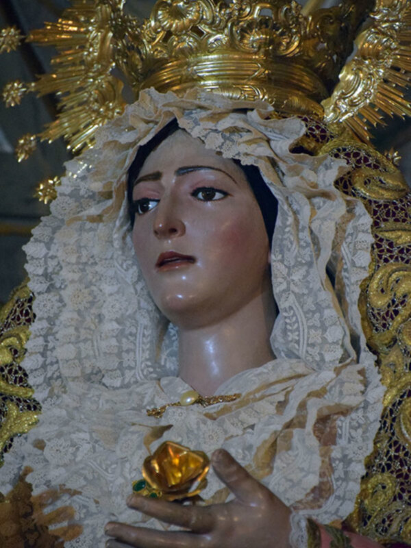 Detalle de una imagen de la Virgen con una corona dorada y ropa bordada.