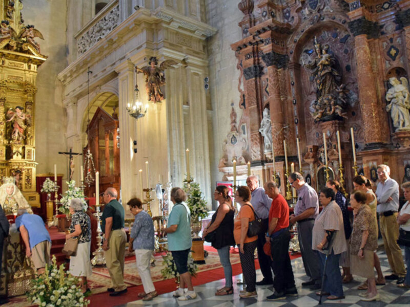 Visita guiada en una majestuosa iglesia con decoración barroca y visitantes admirando el interior.