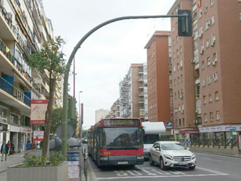 Vehículos circulando en una calle urbana con edificios residenciales al fondo.