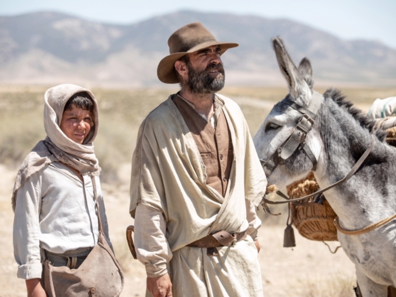 Un hombre y un niño con sombrero y burro en un paisaje desértico.