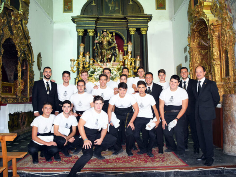 Grupo de jóvenes en uniforme blanco posando en el interior de una iglesia con un altar dorado y estatuas religiosas en el fondo.