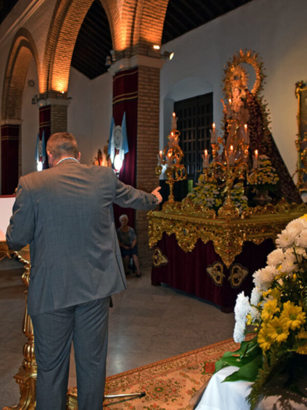 Un hombre en traje dirige su atención hacia un altar adornado con flores y candelabros en una iglesia.