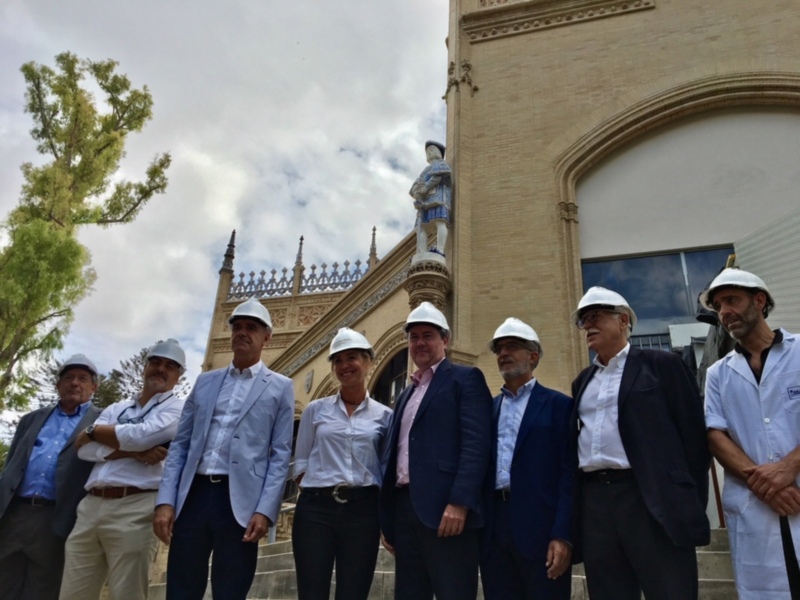 Equipo de trabajo y autoridades posan frente a una antigua estructura histórica con una estatua en el centro.