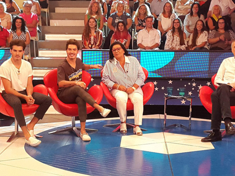Panelistas sentados en sillas rojas en un escenario con audiencia en el fondo.