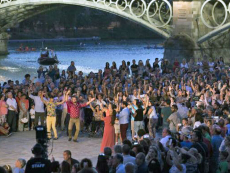 Una multitud de personas disfrutando de un evento al aire libre en un puente junto al río, con un público numeroso y entusiasmado.