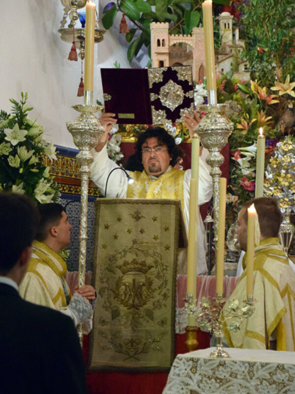 Un sacerdote oficia una ceremonia religiosa con velas y ornamentación festiva.