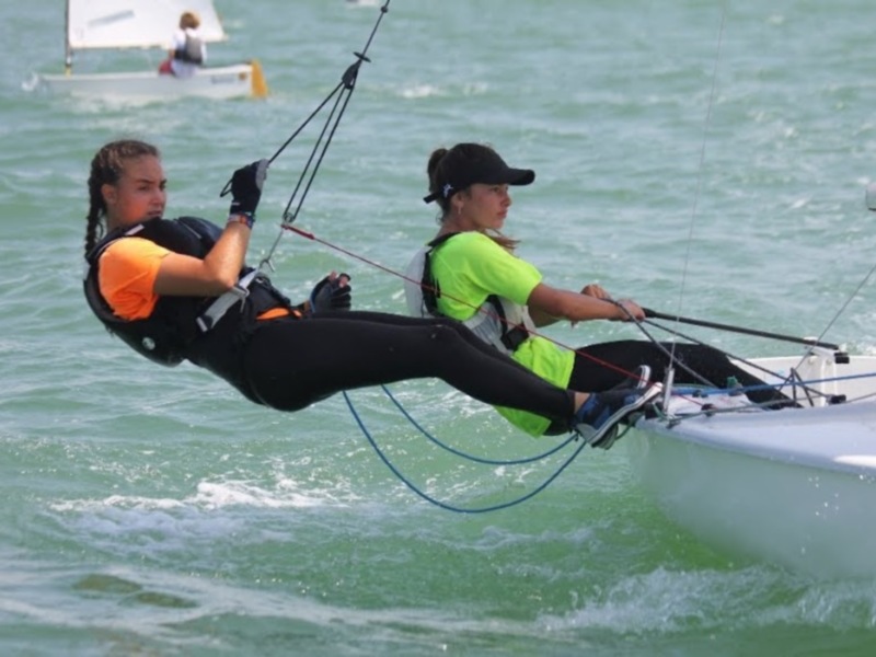Dos jóvenes competiendo en vela, maniobrando un velero en el mar.