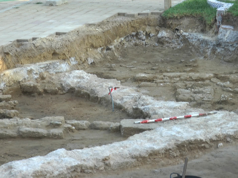 Excavación arqueológica en un entorno urbano, con evidencias de estructuras antiguas y herramientas de excavación en el suelo.