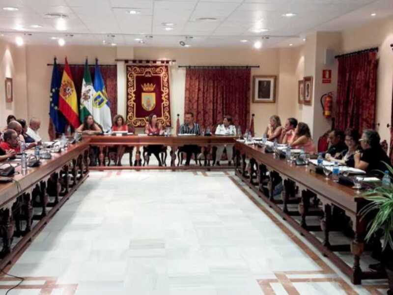 Sala de reuniones con una mesa larga y varias personas sentadas, rodeada de banderas y decoración oficial.