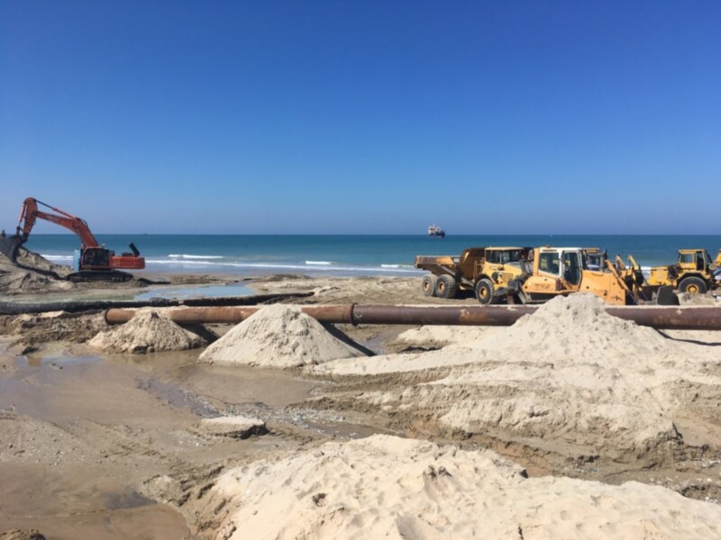 Trabajos de construcción costera con maquinaria pesada en una playa.