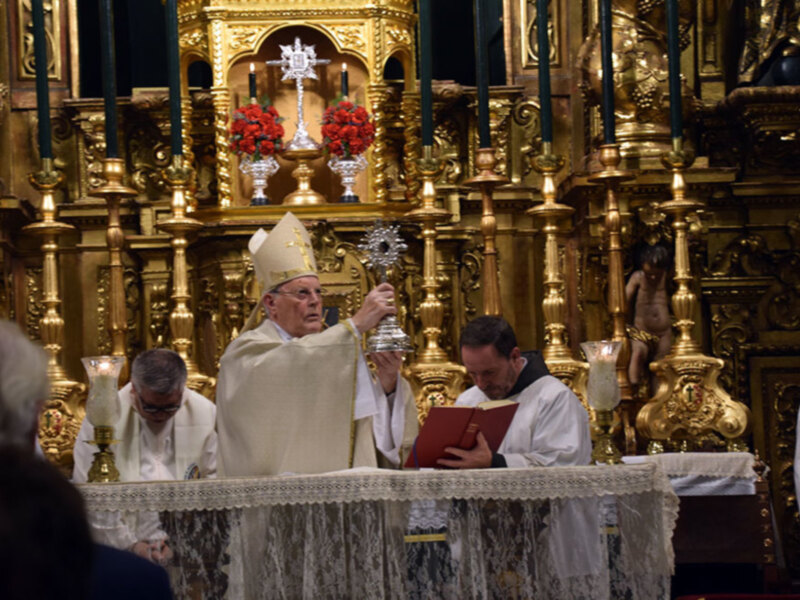 Celebración religiosa en un altar ornamental con sacerdotes en trajes blancos y un ornamento central dorado.