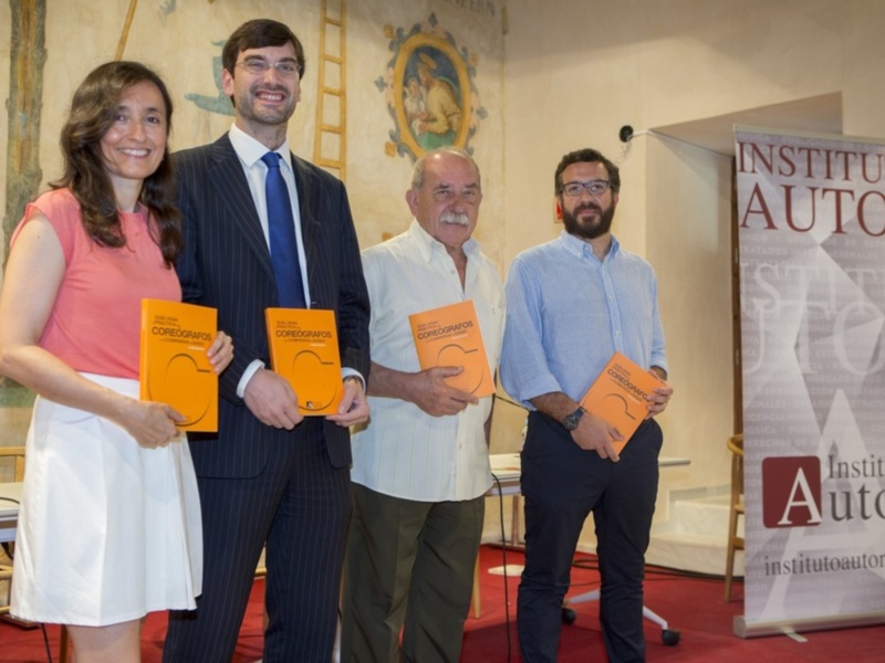 Tres personas sonrientes en una conferencia, sosteniendo libros con el título 'Coreógrafos' en una sala con decoración y un cartel del Instituto Autor en el fondo.