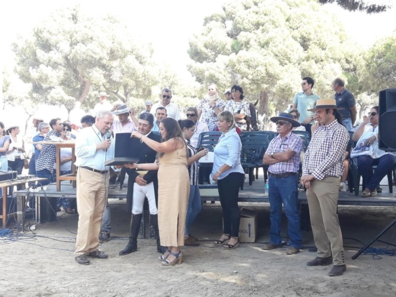 Celebración al aire libre con un grupo de personas en un escenario rodeado de árboles.