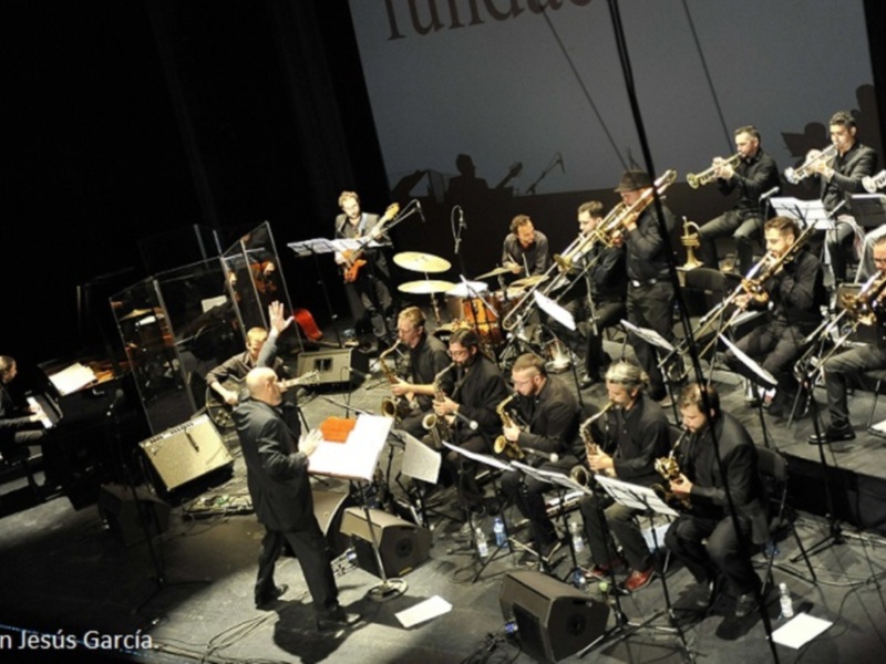 Orquesta de jazz en concierto, músicos tocando instrumentos en un escenario iluminado.