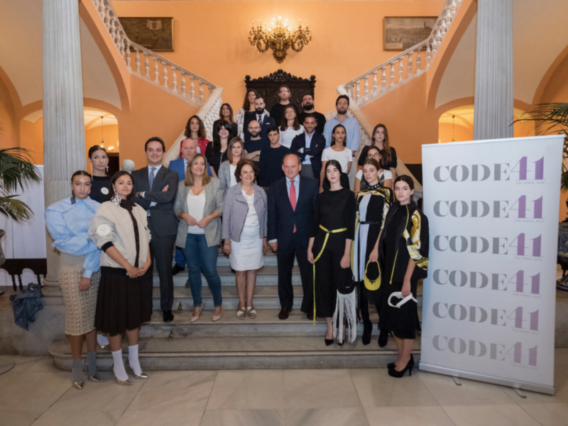 Gruppo di persone in posa per una foto di gruppo in un elegante ambiente interno con scale e decorazioni. Sullo sfondo si legge "CODE41".