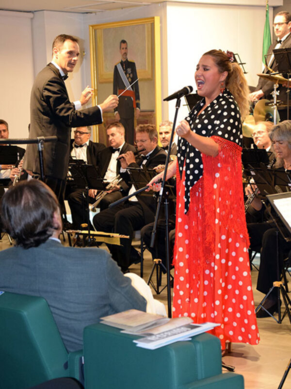 Concierto de música clásica con una cantante en traje flamenco y un director de orquesta dirigiendo.