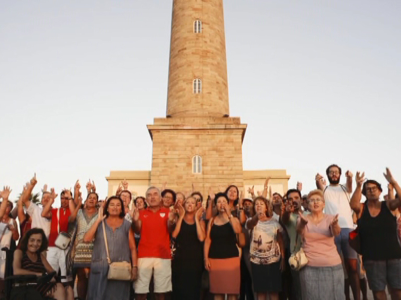 Grupo de personas celebrando frente a un faro en la puesta de sol.