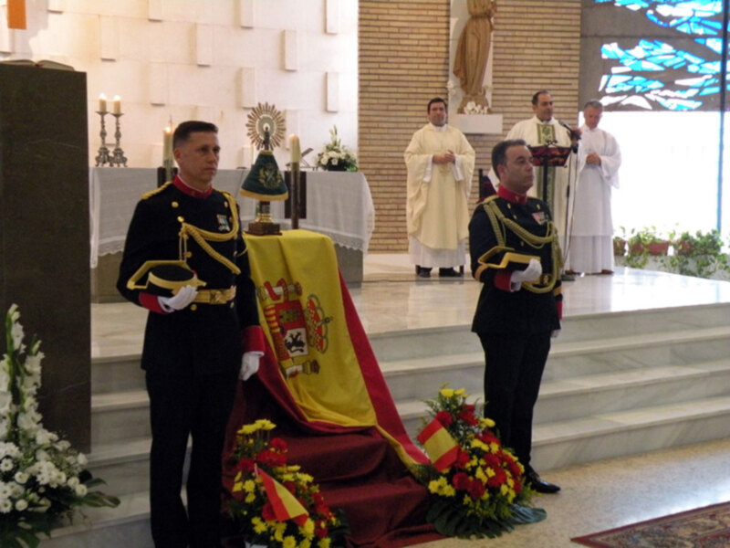 Oficiales militares en uniforme ceremonial en una ceremonia religiosa con sacerdotes y bandera española.