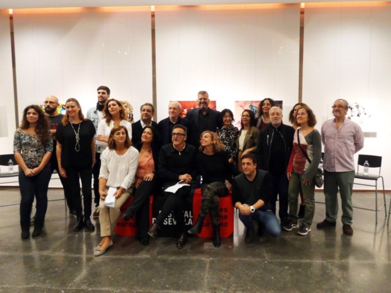 Gruppo di persone in posa per una foto di gruppo in un ambiente interno con opere d'arte sullo sfondo.