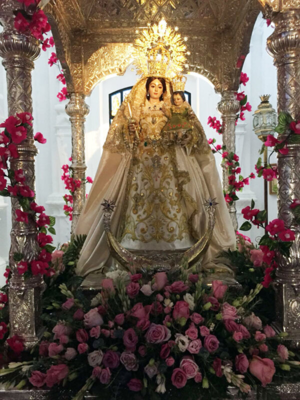 Estatua religiosa adornada con flores y vestidos de oro en un entorno dorado.