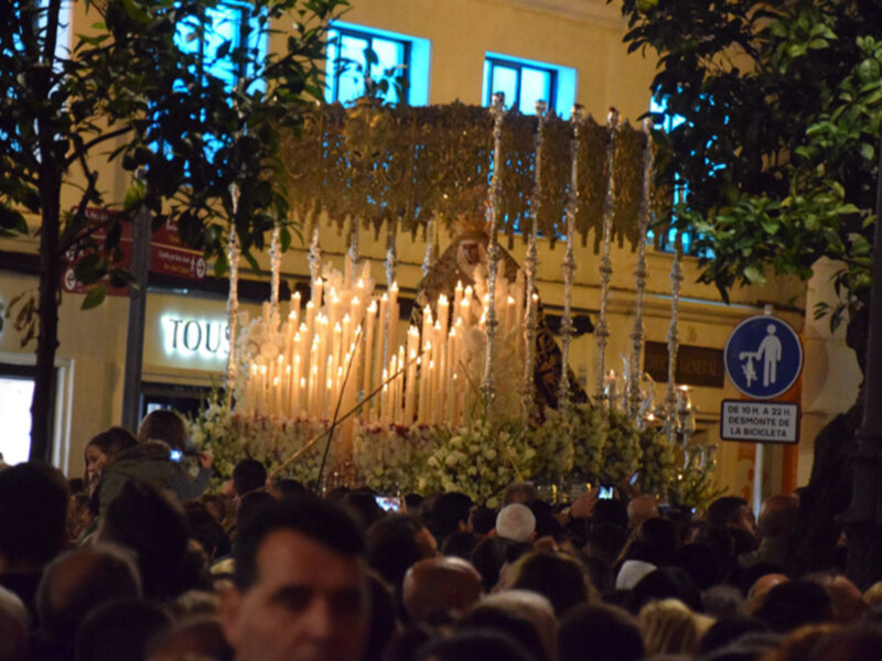 Procesión con candelabros y flores en una calle iluminada por las velas.
