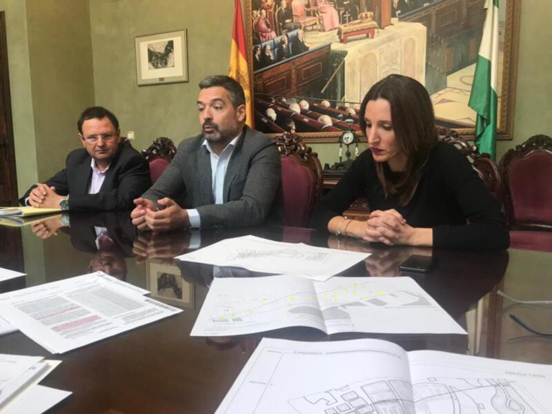 Dos personas sentadas en una mesa con documentos y una bandera española en el fondo.