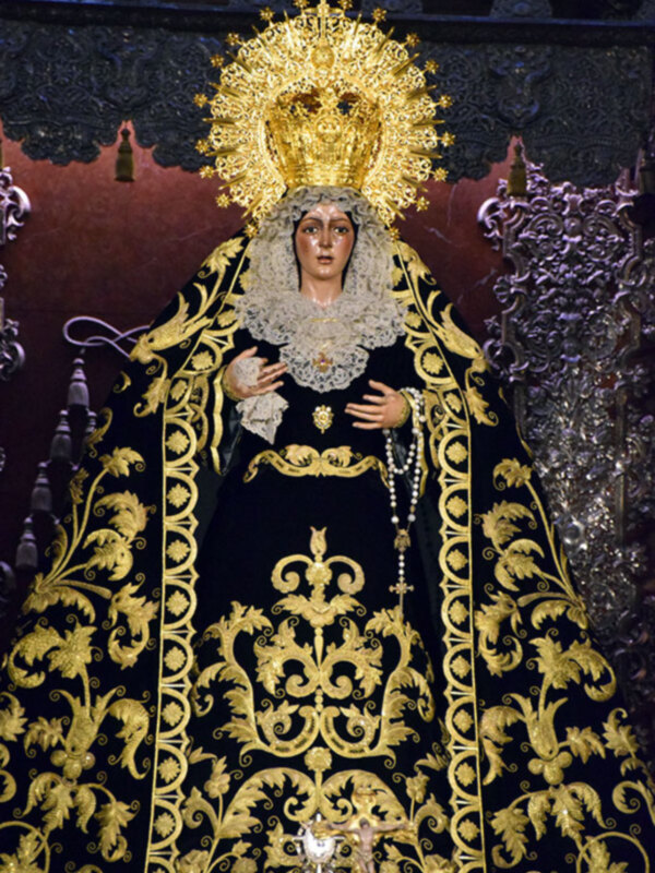 Figura religiosa con vestimenta negra y dorada, coronada con una gran corona de oro, representando a la Virgen de la Soledad.