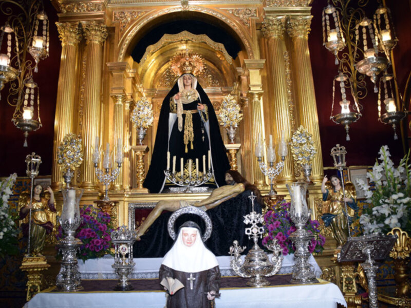 Altar con estatua de la Virgen de la Amargura en un entorno ornamental dorado y con flores.