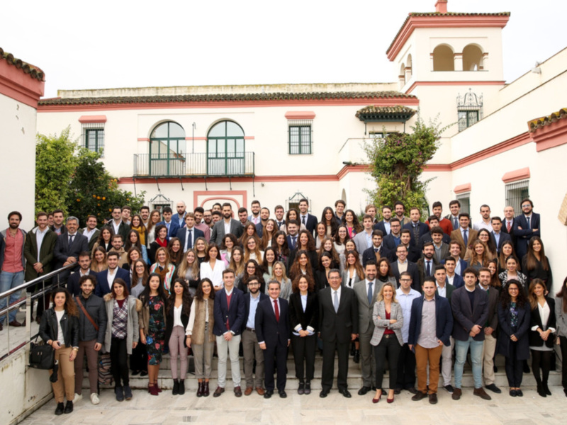Grande grupo de personas posando para una foto en un patio con edificio histórico en el fondo.