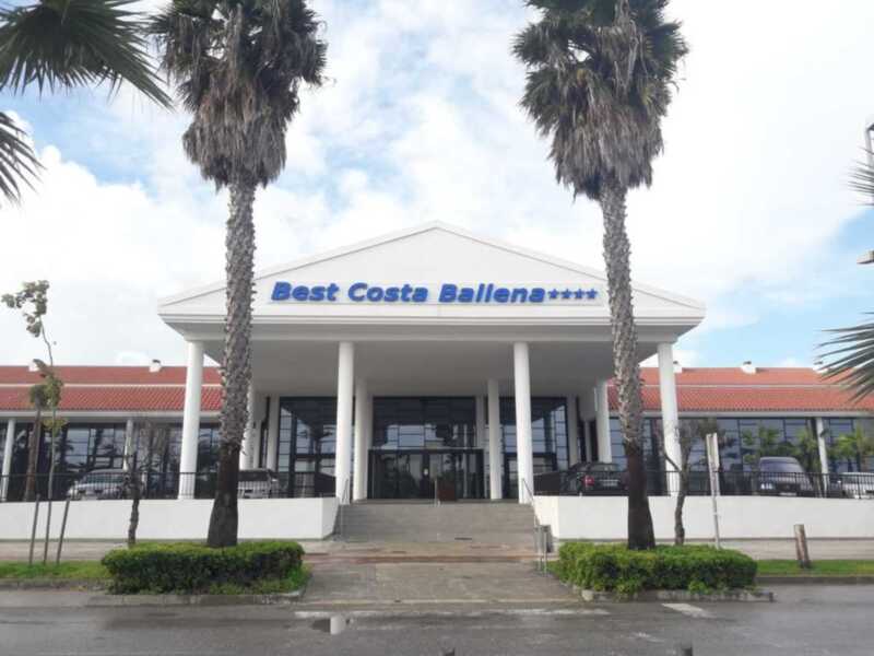 Entrada principal del Best Costa Ballena****, con palmeras y un cielo azul claro.