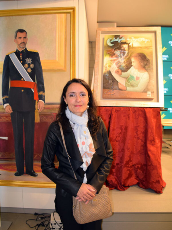 Una mujer posa frente a una imagen de un hombre en uniforme y una pintura de un bebé en un entorno formal.