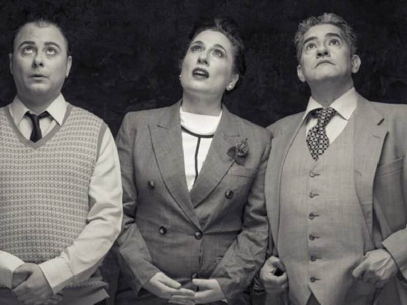 Tres personas mirando hacia arriba en una escena de teatro o cine, con un fondo oscuro que enfoca la atención en ellos.