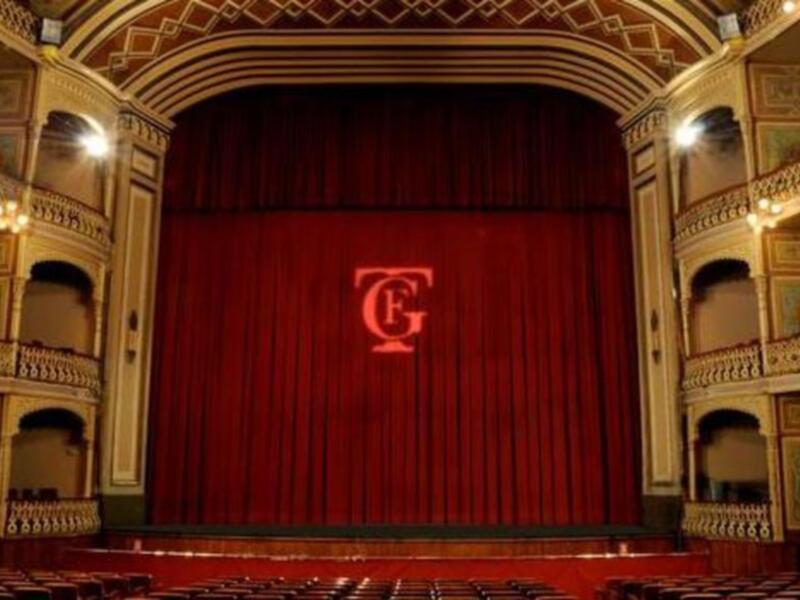 Interior of a grand theater with ornate red curtains and intricate architectural details.