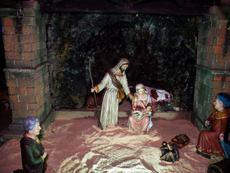 Representación de la Natividad en un belén, con figuras de la Virgen María, el Niño Jesús y San José en un entorno de casas de arcilla y rocas.