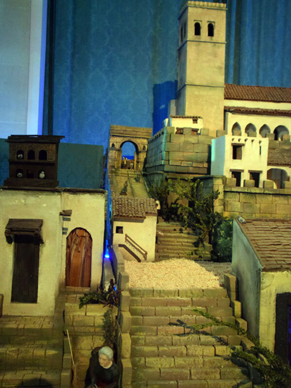 Miniatura de una escena histórica con edificios y personajes en un escenario iluminado.