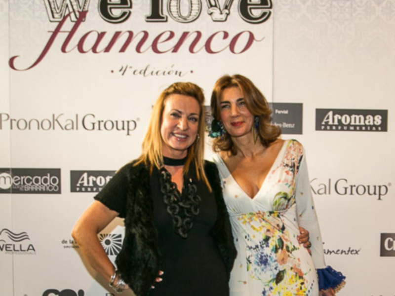 Dos mujeres posan juntas en un evento de la '4ª edición de We love Flamenco' con logos de 'PronoKal Group' y 'Aromas' en el fondo.