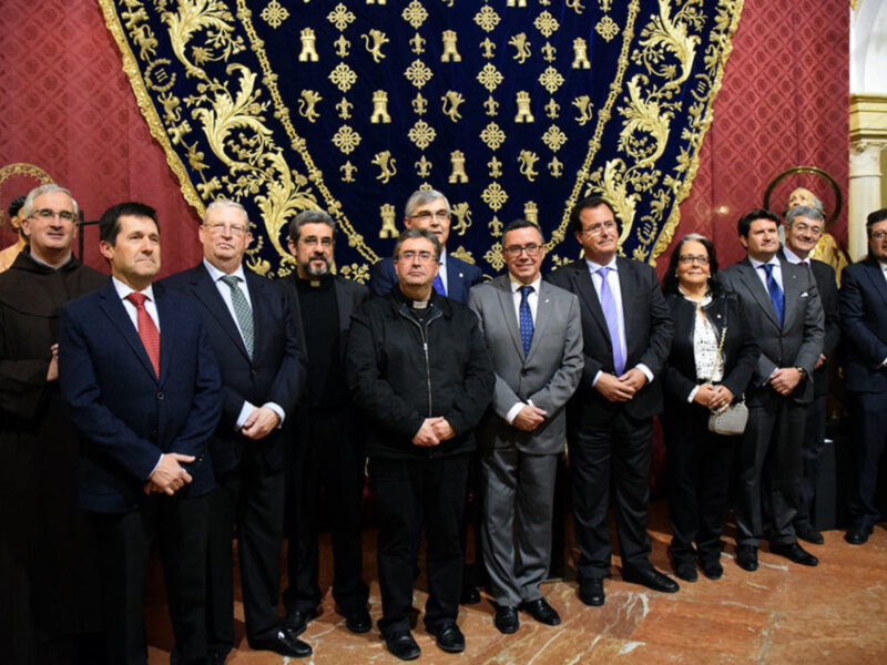 Grupal de personas en una ceremonia formal frente a un fondo ornamental con estandartes religiosos.