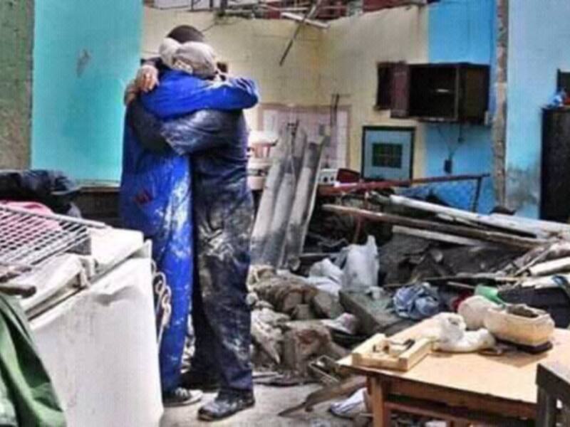 Dos personas abrazándose en un entorno destruido, posiblemente tras un desastre natural.