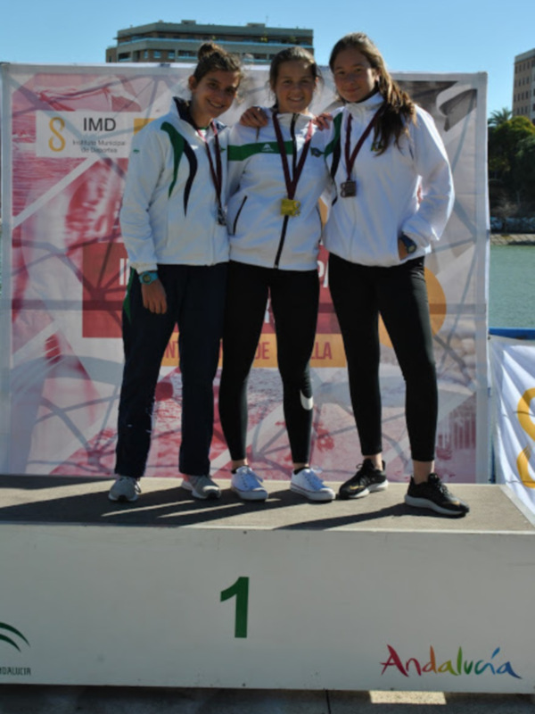 Tres atletas posan con sus medallas de oro en un podio, con un fondo que incluye una bandera y el nombre 'Andalucía'.