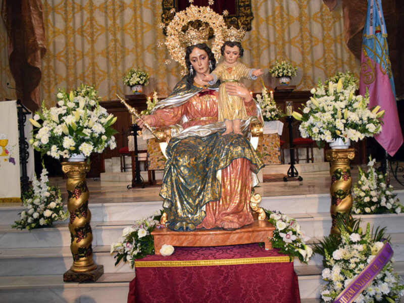 Immaculate statue of the Virgin Mary and Child Jesus adorned with gold and surrounded by floral decorations in a church setting.