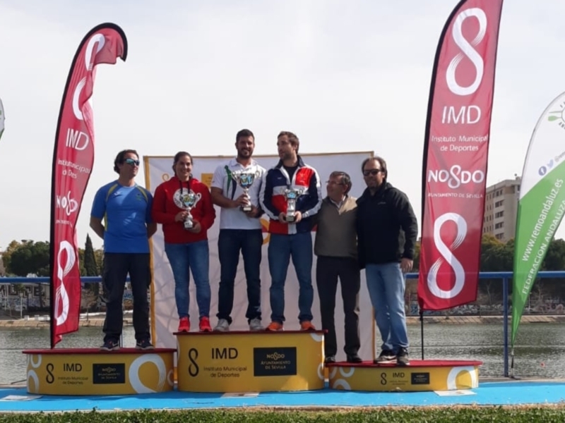 Podio de una competición de remo en Sevilla, con representantes y trofeos en el centro.
