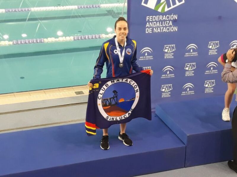 Medalla de oro en la piscina, con un trofeo y un banner del Club Natación Sinlucan. Federación Andaluza de Natación en el fondo.
