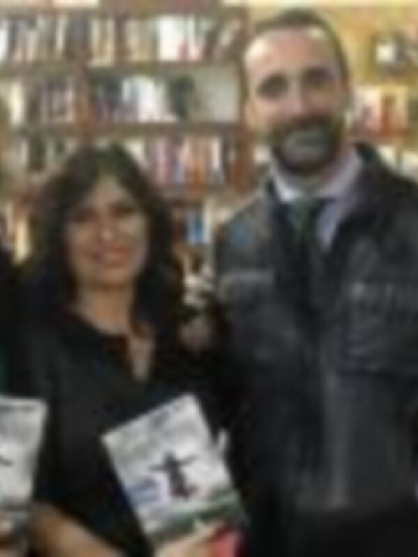 Tres personas en una biblioteca, sonriendo y posando con libros en las manos.