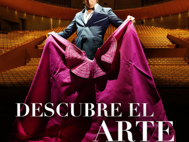 Una persona con un vestido rojo en un escenario con asientos vacíos, promoción de la Feria de Arte de Abril 2019.